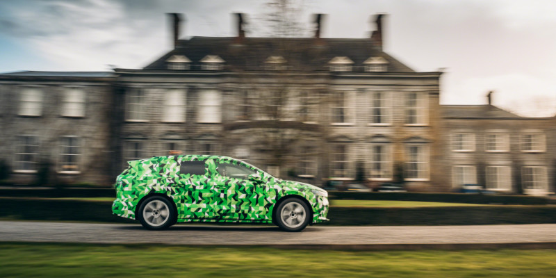 A camouflaged car drives past a big house.